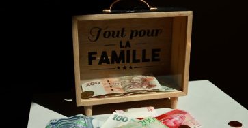 A wooden box with money and 'Tout pour la Famille' text, symbolizing family savings.