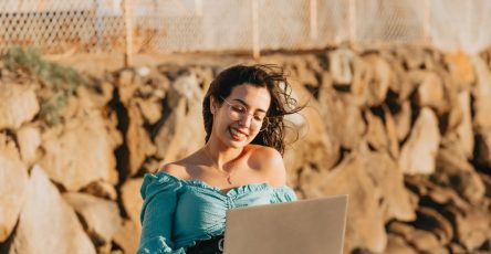 Woman enjoying remote work with laptop outdoors, smiling on a windy day.