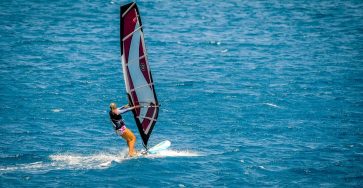 Woman windsurfing on open blue ocean, capturing the thrill and beauty of water sports.