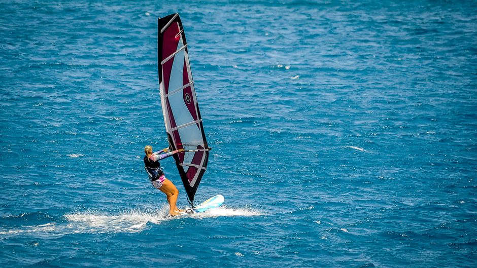 Woman windsurfing on open blue ocean, capturing the thrill and beauty of water sports.